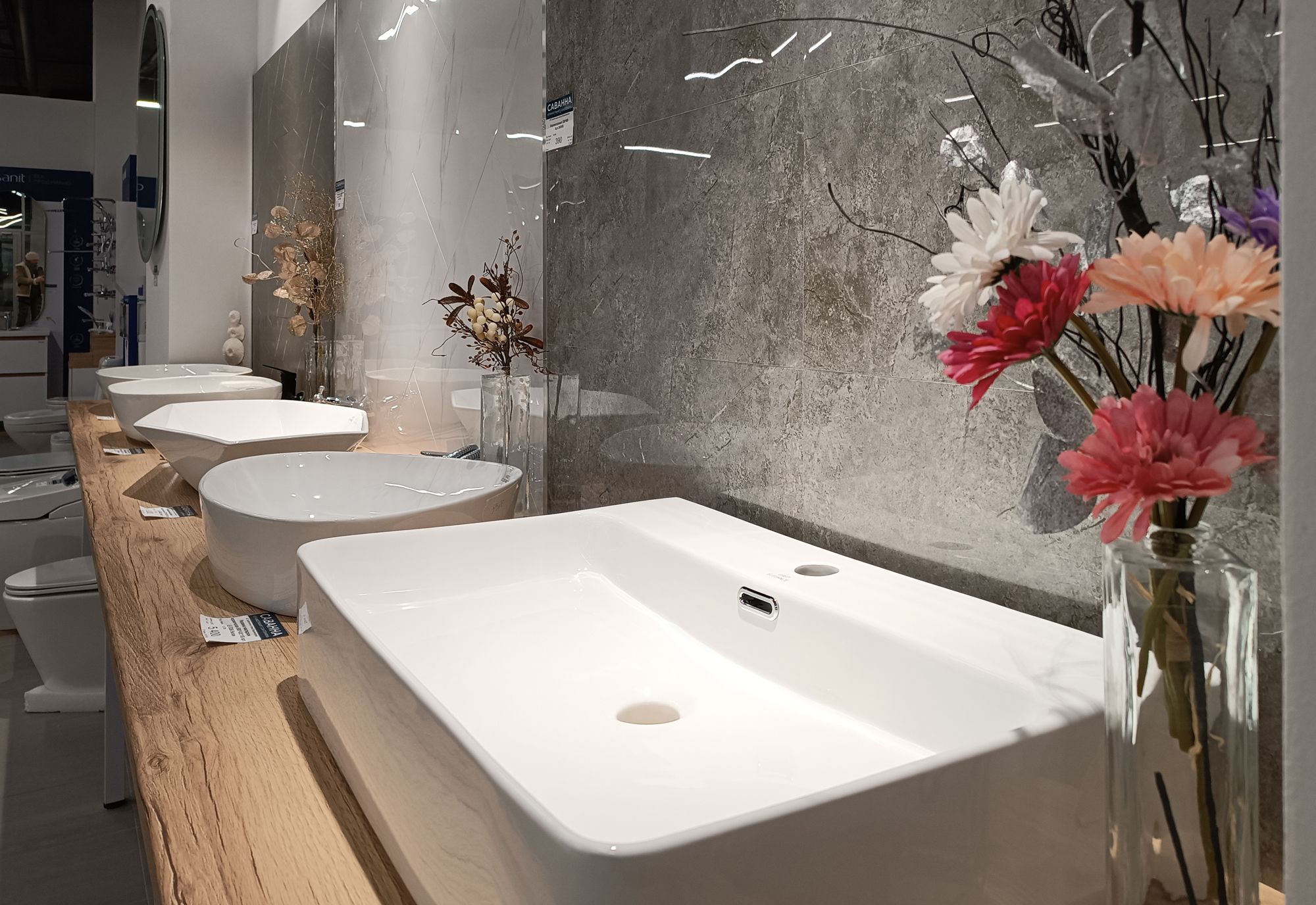 A row of modern white ceramic bathroom sinks on a wooden counter in a showroom.